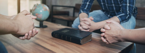Christian friends holding hands together surrounded wooden table